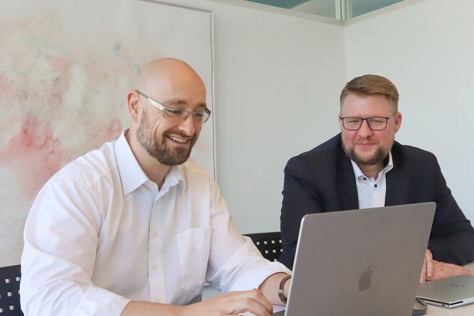 Zwei Personen sitzen vor einem PC und arbeiten.